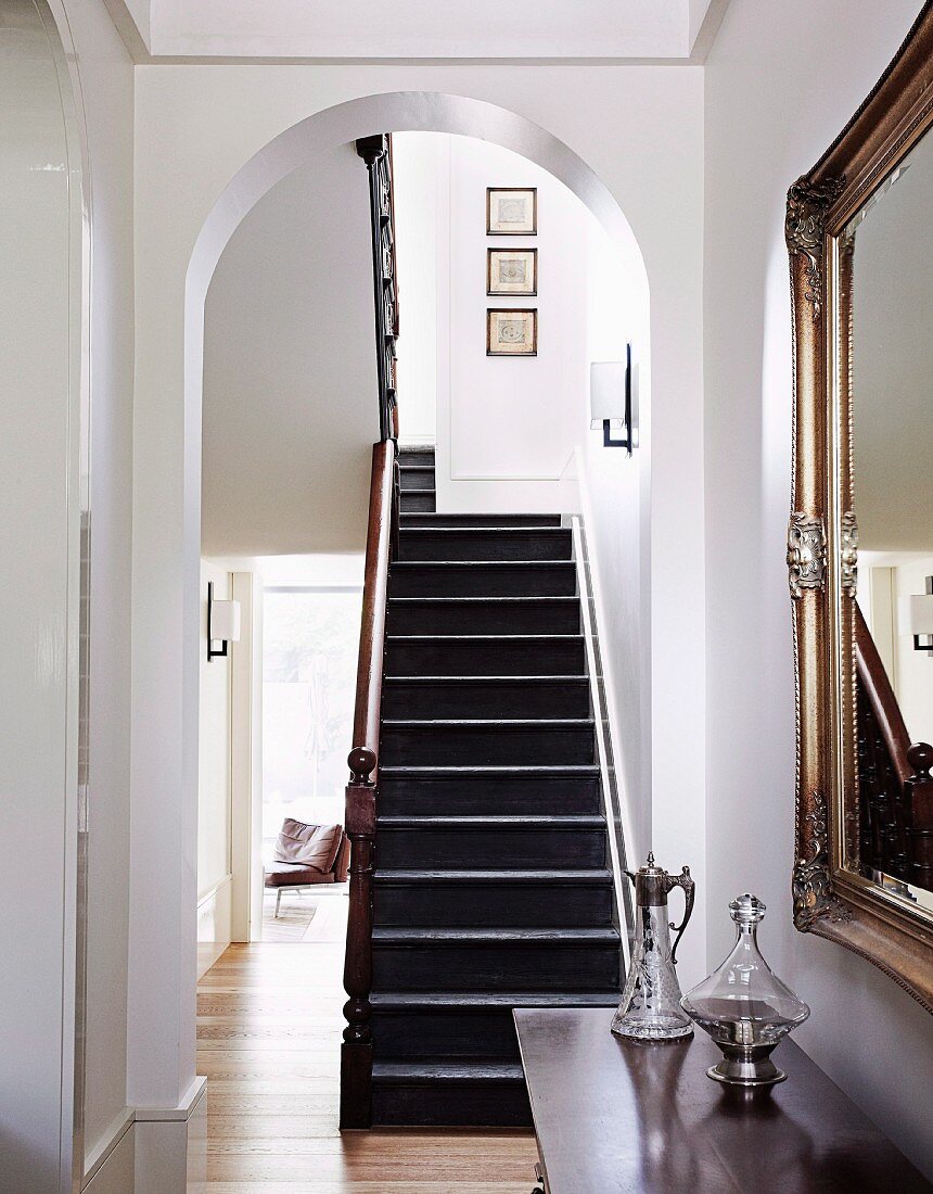 Treppenaufgang in Wohndiele mit elegantem Garderobenspiegel und antiken Glaskaraffen auf einer Kommode