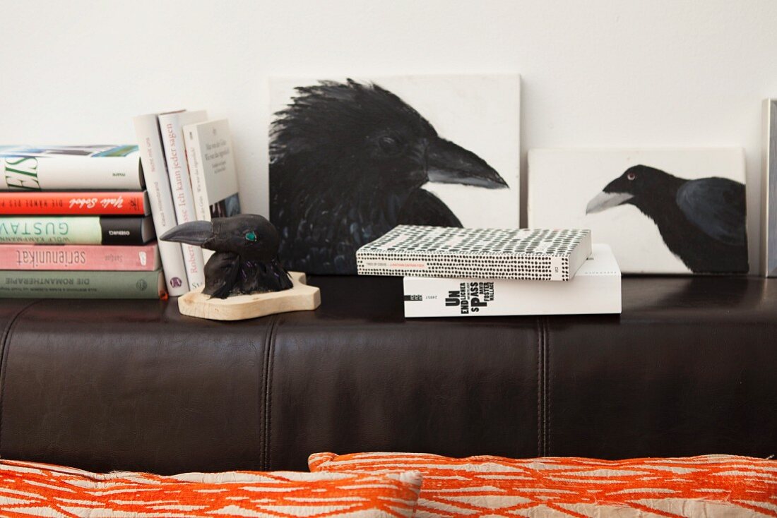 Picture of crow, picture of rook and stacked books on backrest of black leather couch