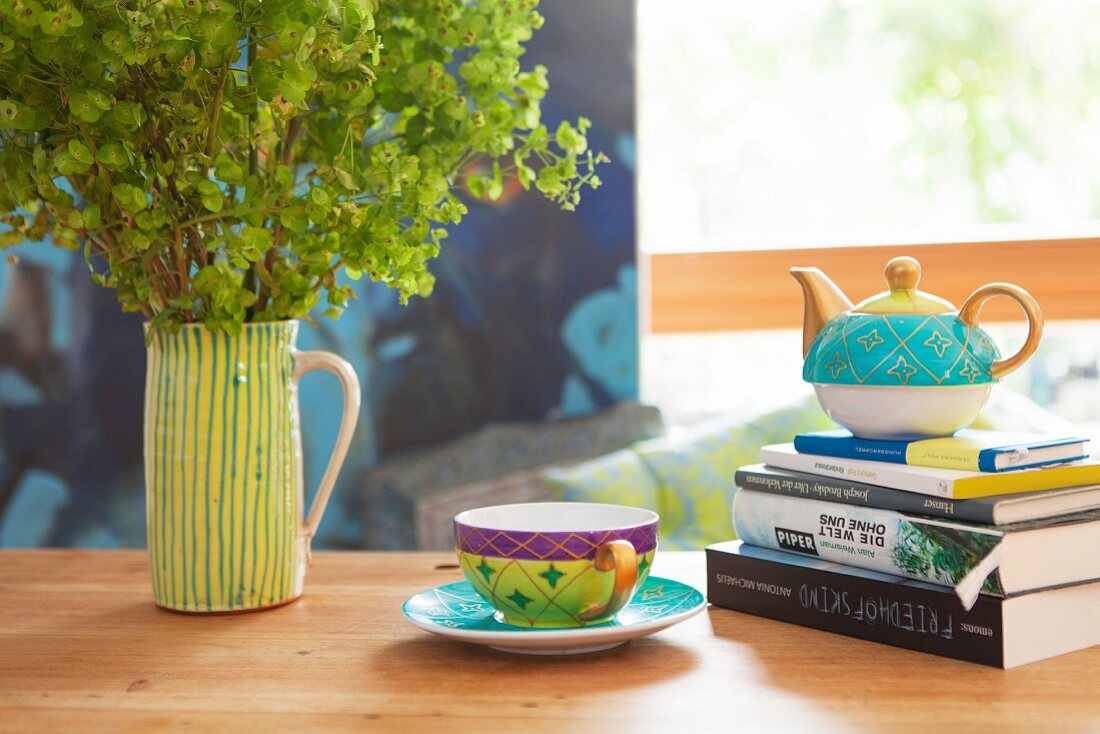 Teacup next to teapot on stack of books and ceramic jug of lady's mantle