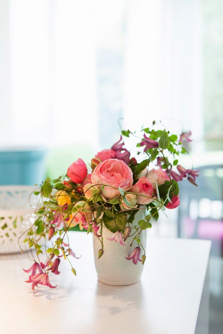 Bouquet of fragrant English roses, clematis and other flowers in white vase on table