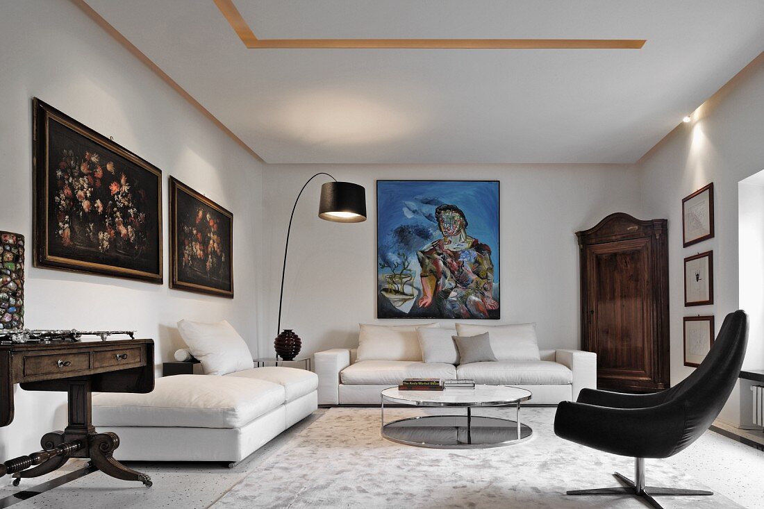 Weisses Wohnzimmer im Stilmix mit antiken und modernen Elementen; an der Wand antike Blumenstilleben und ein modernes Ölgemälde