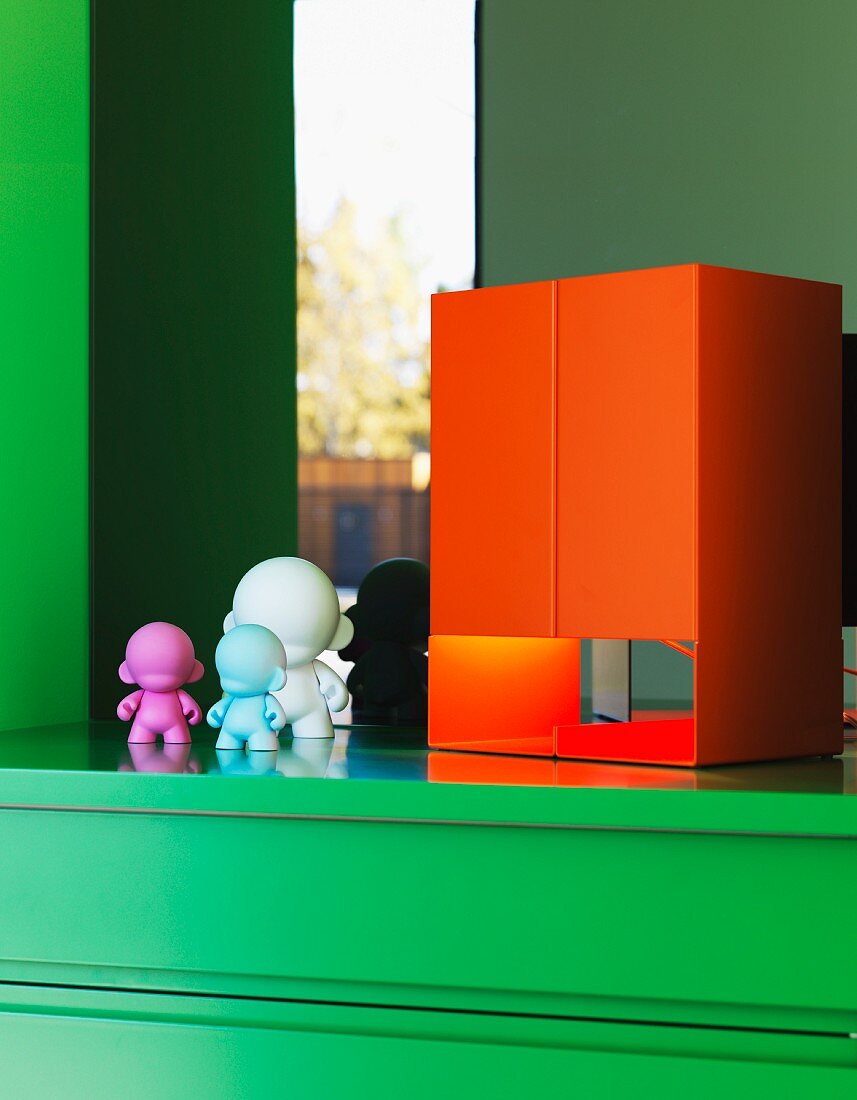 Orange, cubic table lamp and small plastic figurines on green cabinet