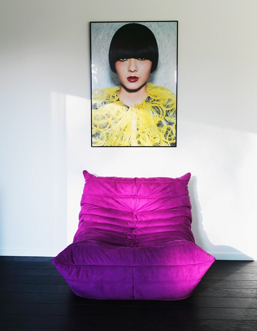 Violetter Sitzsack auf dunklem Holzboden, vor Wand mit gerahmter Damen-Foto