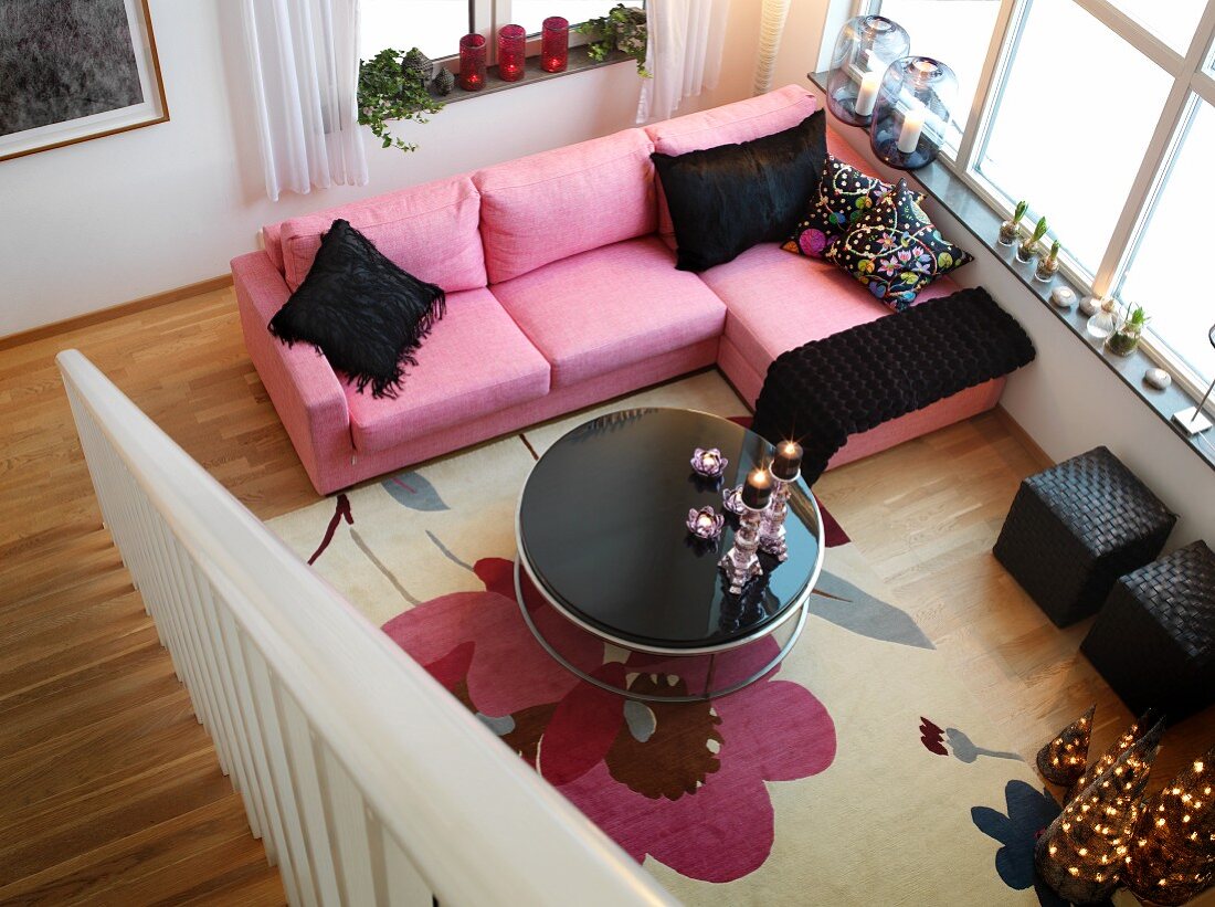 Vom oberen Treppenabsatz gesehener Wohnraum mit Sofa in Pastellpink, schwarzen Accessoires und vorweihnachtlicher Kerzendekoration
