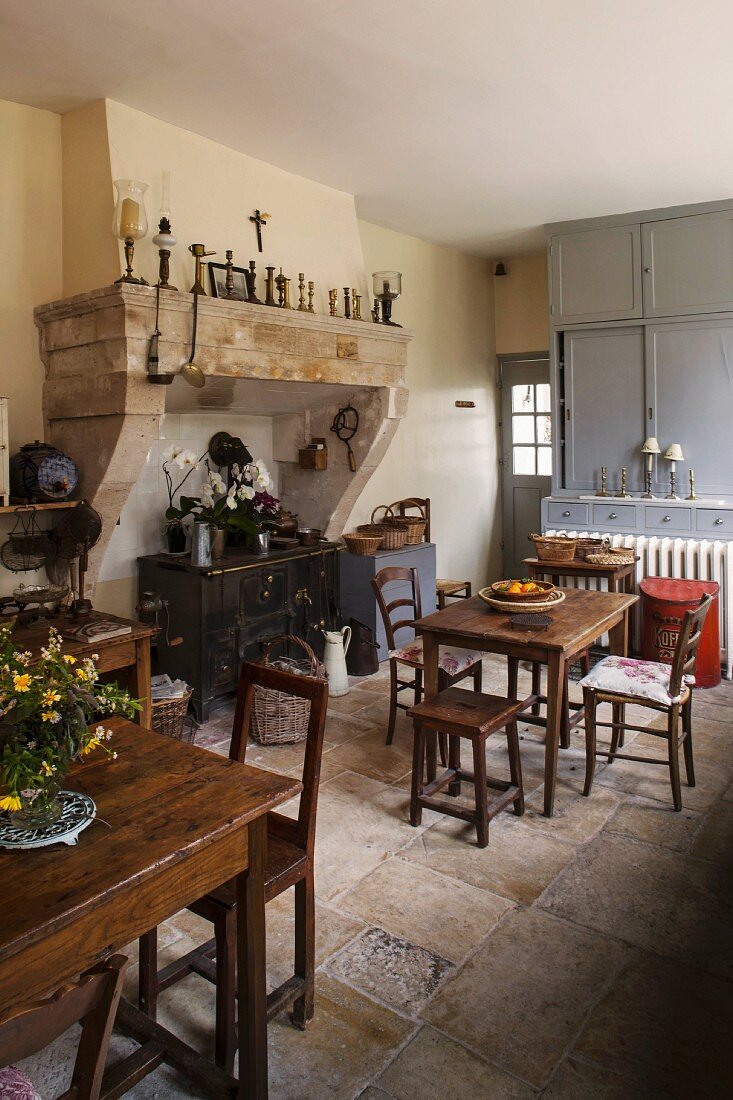 Rustikale Wohnküche mit Holztischen und -stühlen; antiker Holzherd im ehemaligen Kaminabzug