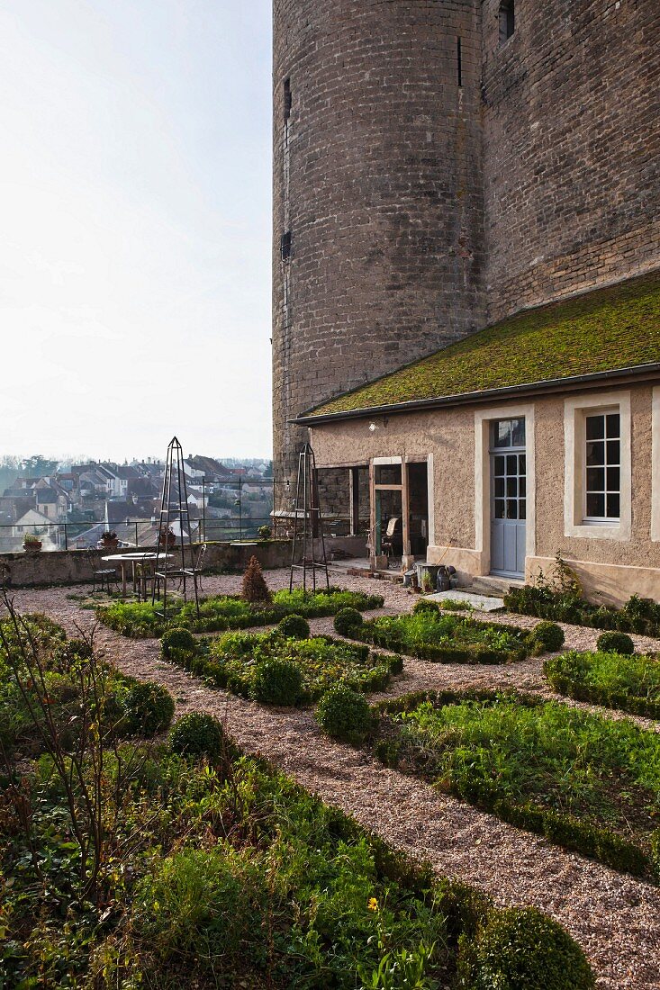 Terrassengarten mit geometrischen Beeten vor historischer Turmfassade mit Wohnhaus
