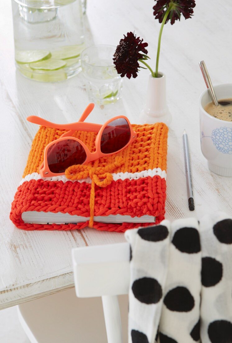 A pair of sunglasses on a knitted book cover in red and orange tones on a white cloth