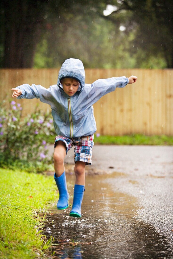 Boy in wellington boots jumping in puddle