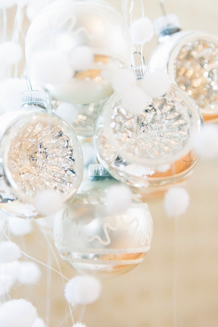 Silberfarbene Weihnachtskugeln und kleine, weiße Flauschkugeln als Schneeflocken-Deko