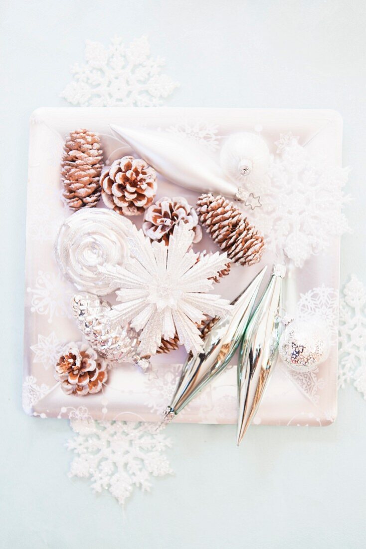 Christmas arrangement of fir cones sprayed white and stylised snowflakes on square dish