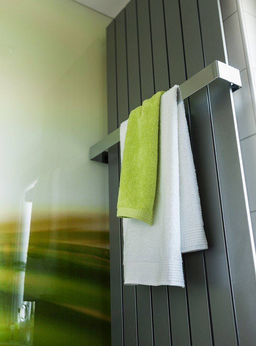 Green and white towels hanging from a rail on a stainless steel towel dryer in a shower area in a modern bathroom
