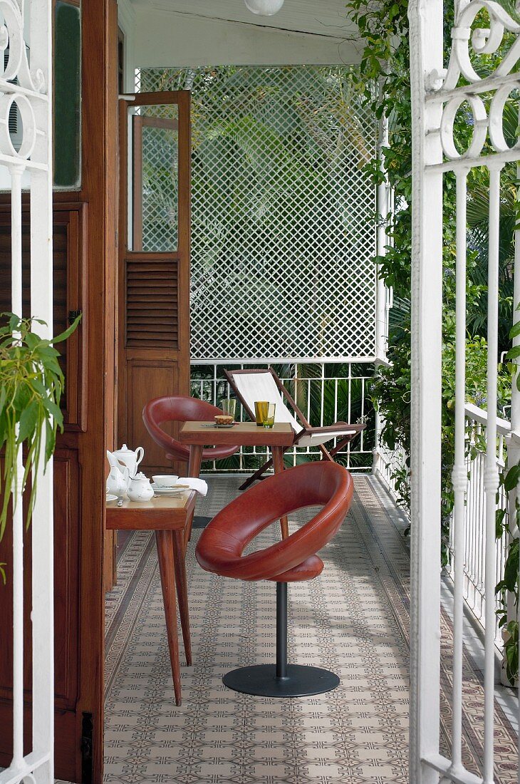 Blick durch offene Balkon Gittertüren auf gedeckte Frühstückstische im Freien, Drehstühle mit braunem Lederbezug und Tische im 50er Jahre Stil auf gemustertem Fliesenboden