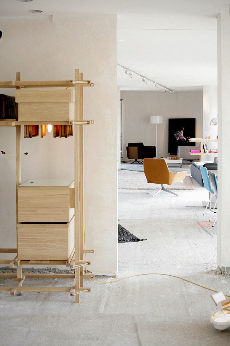 Schlichtes Holzregal mit Boxen in Selbstbauweise, seitlich offener Durchgang und Blick auf Drehsessel in loftartigem Raum