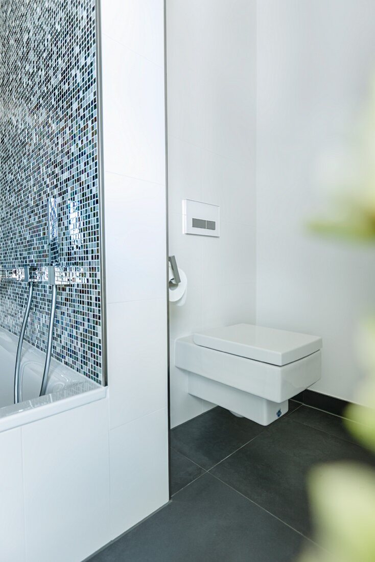WC in gradlinigem, modernem Design, diskret in eine Nische hinter der Badewanne gesetzt