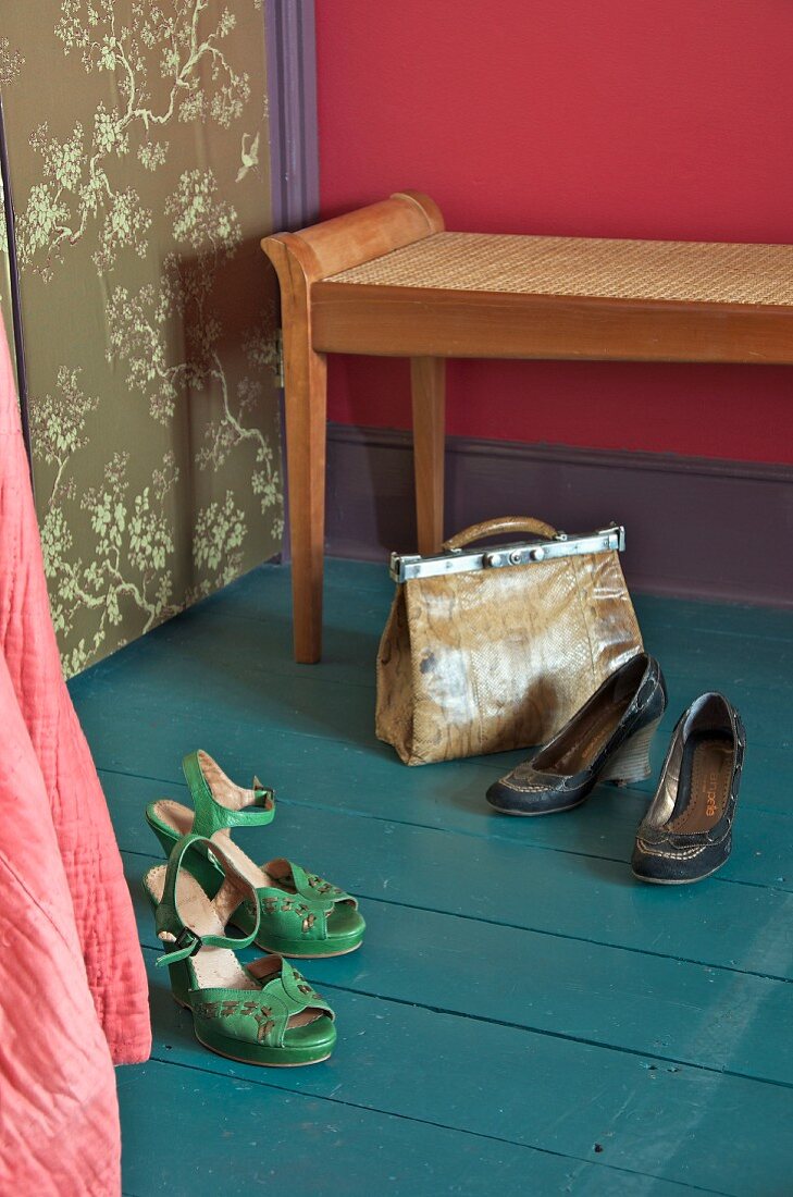 Damenschuhe und Handtasche auf petrolfarbenem Dielenboden, antike Kleiderbank mit Sitzgeflecht vor pinkroter Wandtönung
