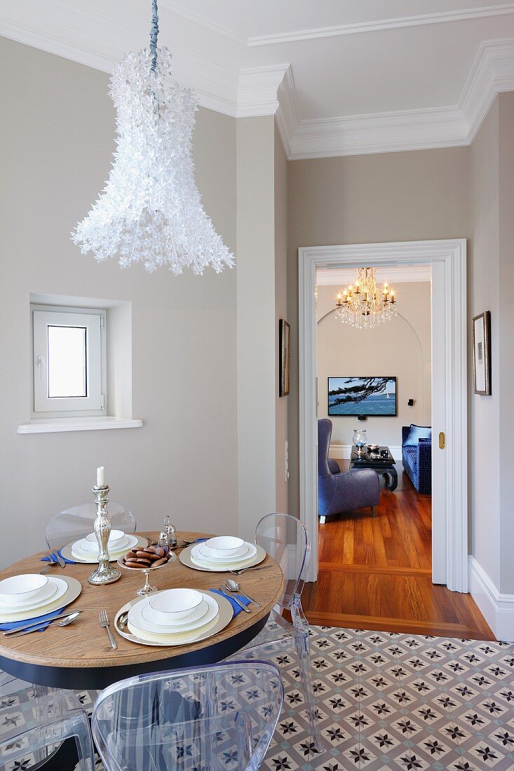 Kunststoff Stühle um gedeckten Tisch, unter gefiederter Hängeleuchte, im Esszimmer mit gemustertem Fliesenboden, Blick durch offene Tür in Wohnraum