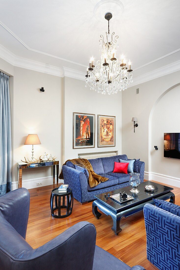 Blaue Sofa-Garnitur und Lesesessel mit blauem Lederbezug um Couchtisch, unter Kronleuchter in traditionellem Wohnzimmer