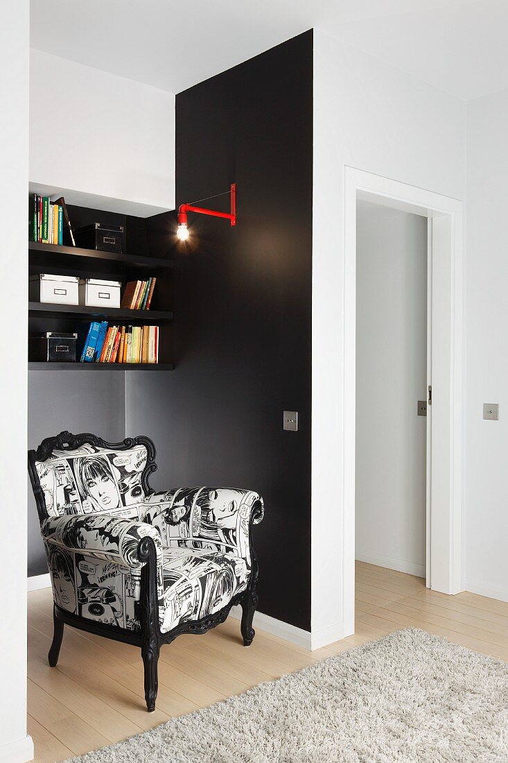 Postmoderner Sessel mit schwarz-weißem Bezug, in schwarz getönter Nische vor Wand mit Regal