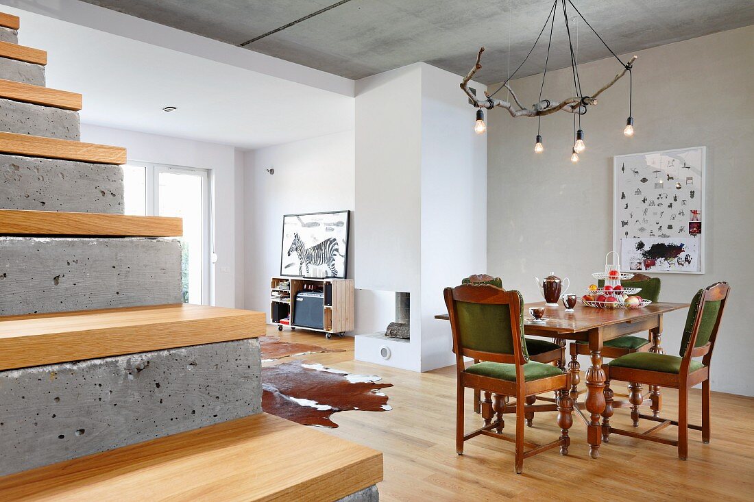 Eichenmöbel mit gedrechselten Beinen und rustikale Ast-Leuchte im offenen, modernen Wohnraum; Sichtbetonstufen mit Holzbelag im Vordergrund