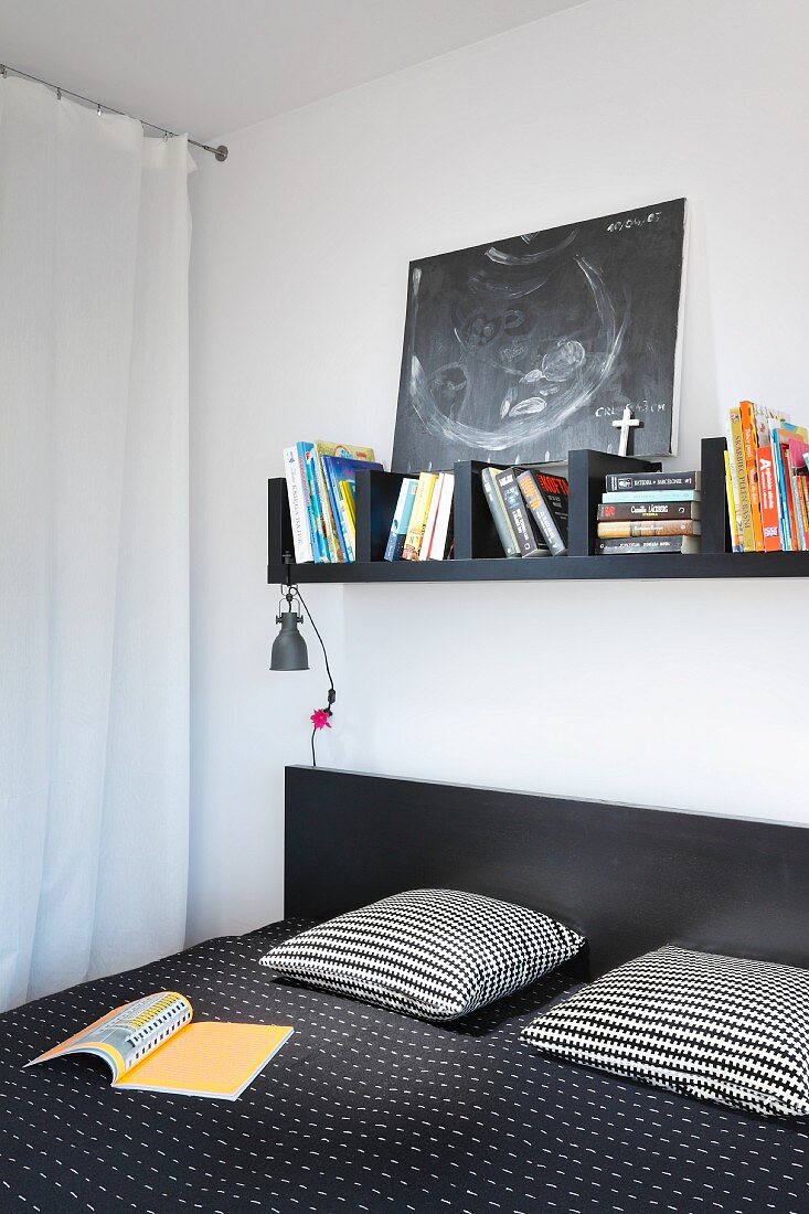 Black bookshelf above double bed with black and white patterned textiles in bedroom