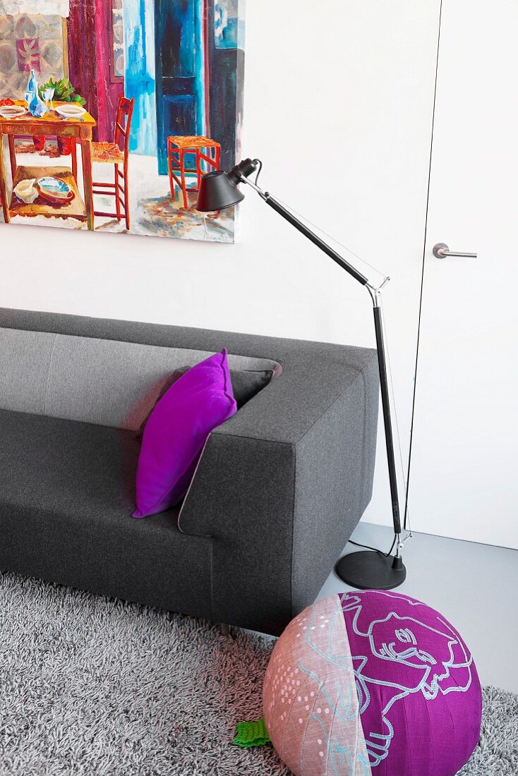 Modern couch with grey felt cover, purple scatter cushion and pouffe in front of black Tolomeo standard lamp