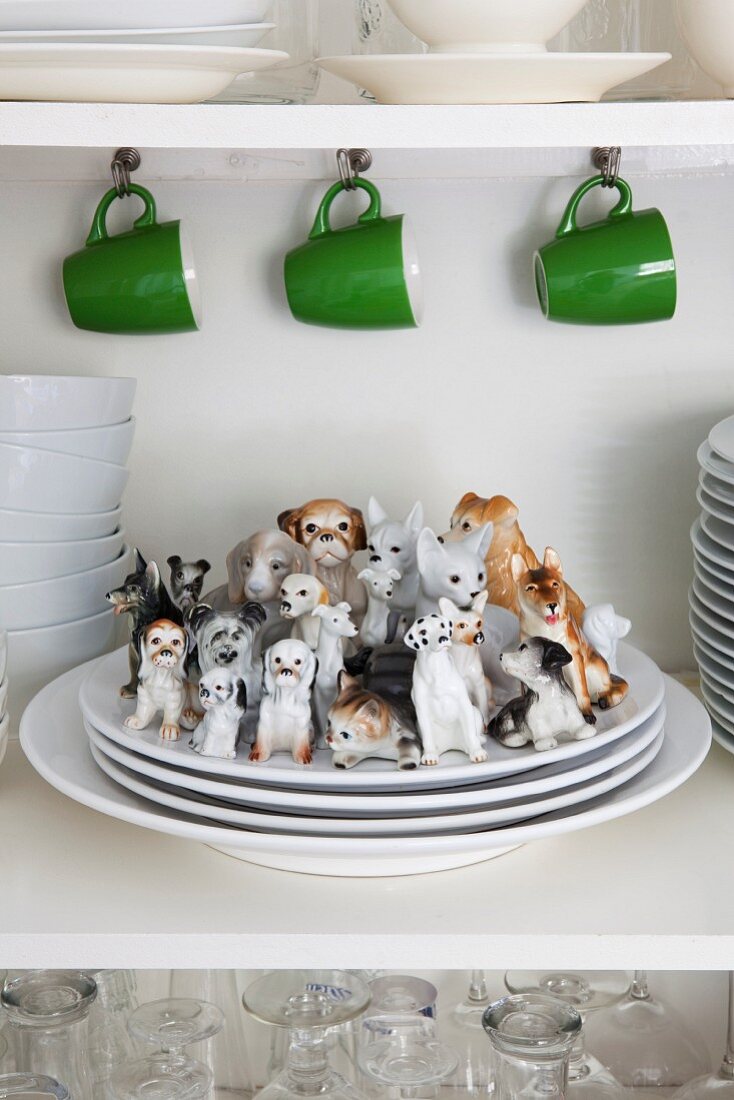 Grüne Kaffeebecher an Hakenleiste und Porzellanhunde auf Tellerstapel in einem Küchenschrank