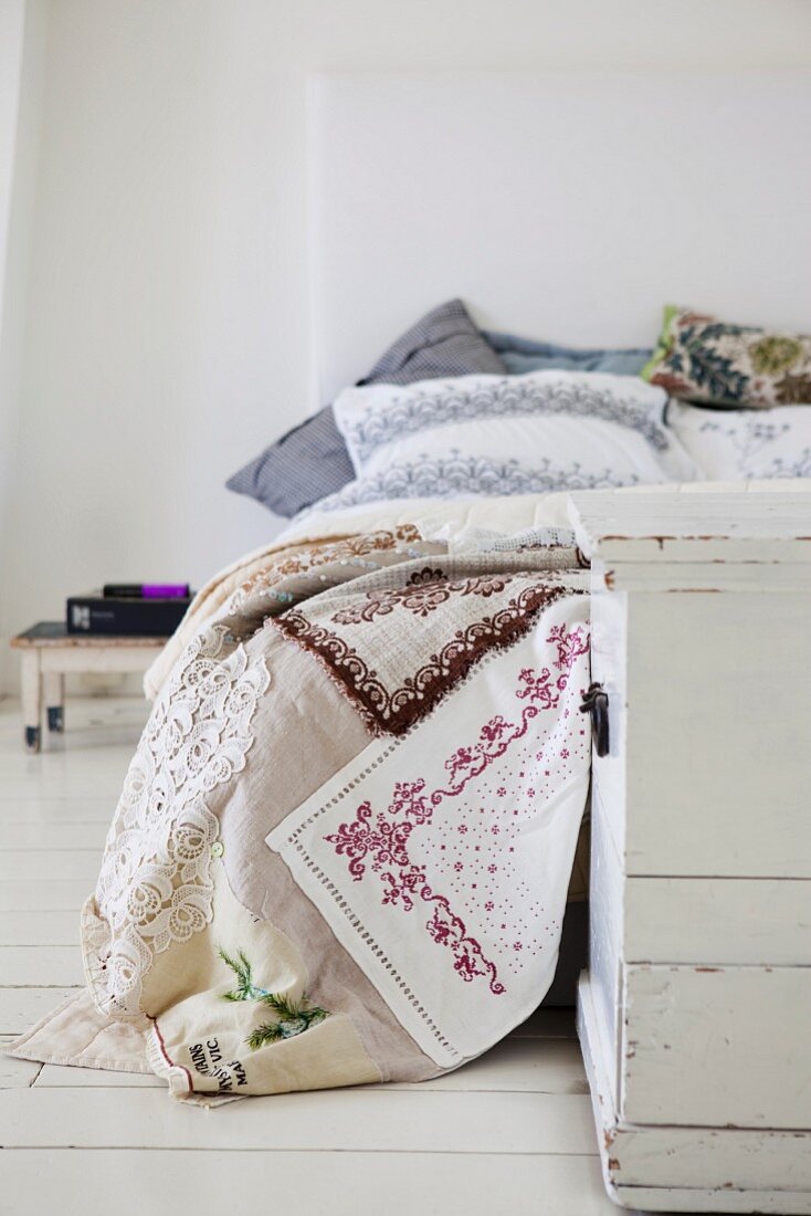 Spitzen-Patchworkdecke und weiße Vintage-Truhe am Fussende eines Bettes