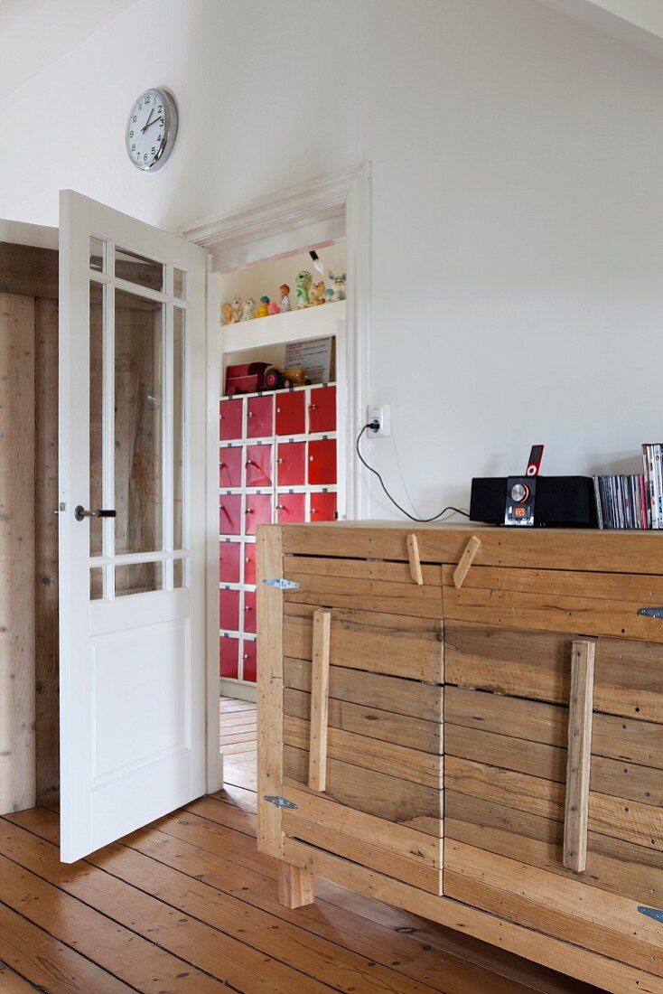 Rustikales Sideboard mit Bretterfronten neben offener Tür zur Diele mit Blick auf Schrank mit roten Türchen