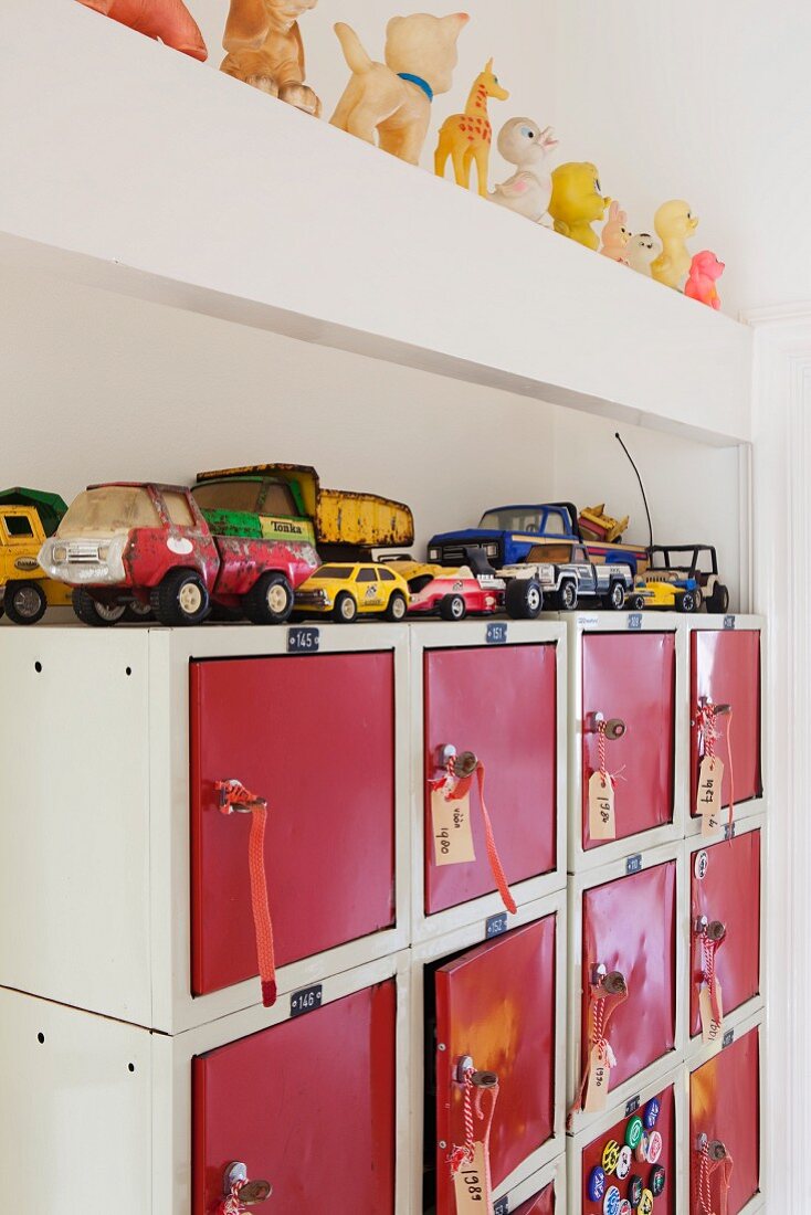 Alte Spielzeugautos auf ausrangiertem Schließfachschrank mit roten Türchen; auf einem Balken aufgereiht eine Sammlung kleiner Qietschtiere