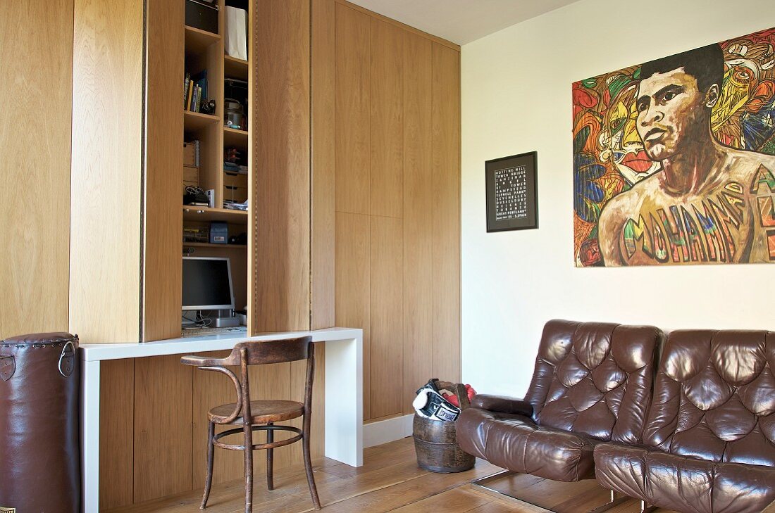 Braune Ledersessel unter Bild, seitlich Einbauschrank aus Holz und integrierter Schreibtisch, davor Thonetstuhl