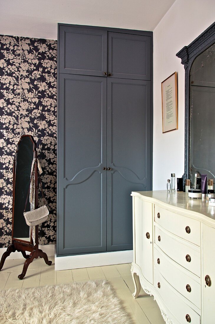 Bedroom with white dressing table and black fitted wardrobe against floral wallpaper