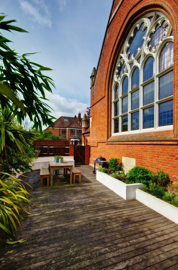 Furnished wooden deck with raised beds adjoining brick facade of Neogothic church
