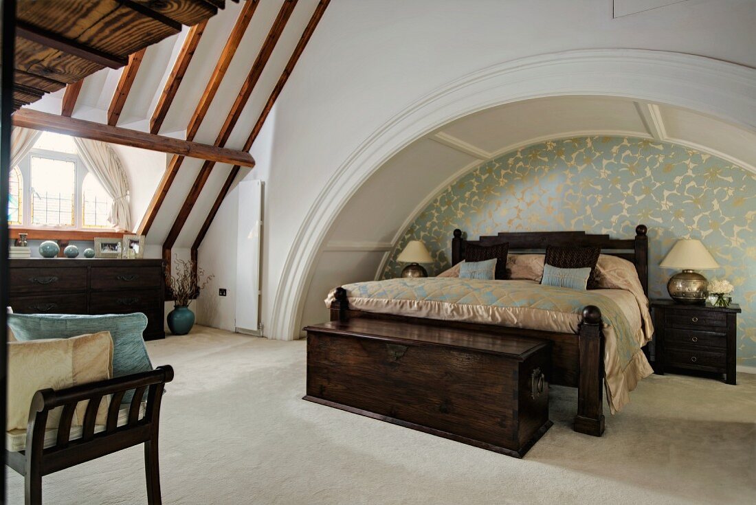 Double bed with dark brown wooden frame in niche formed by arch of vault in converted church interior