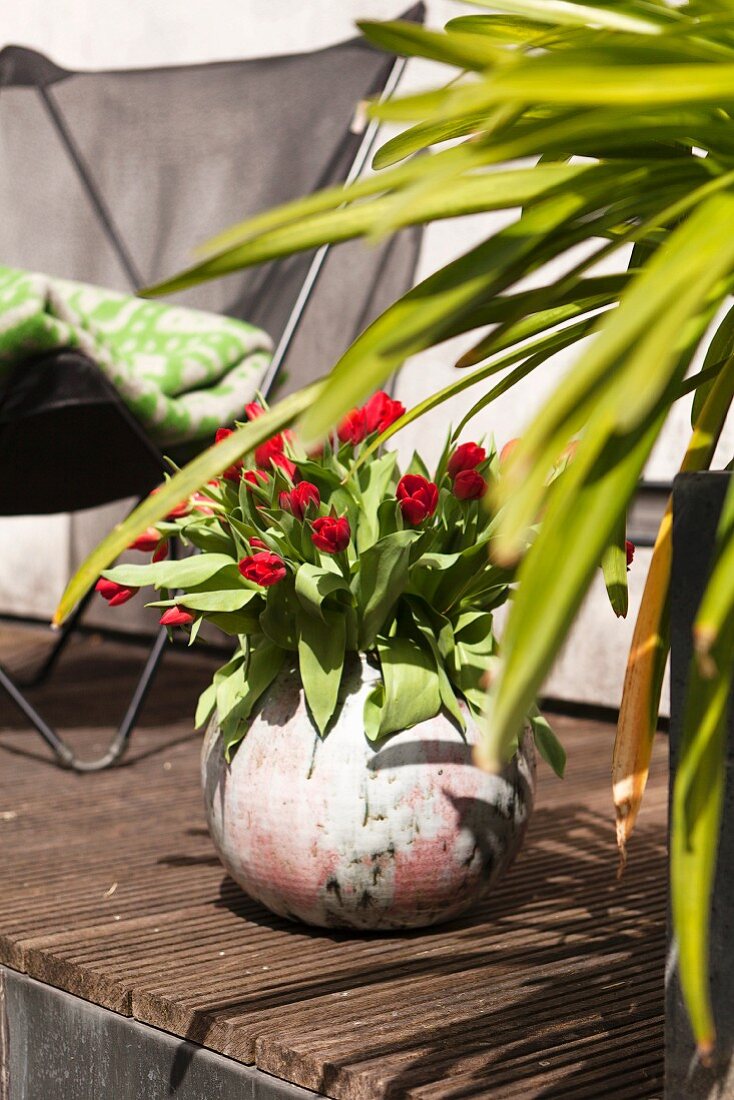 Red tulips in spherical vase on wooden terrace floor
