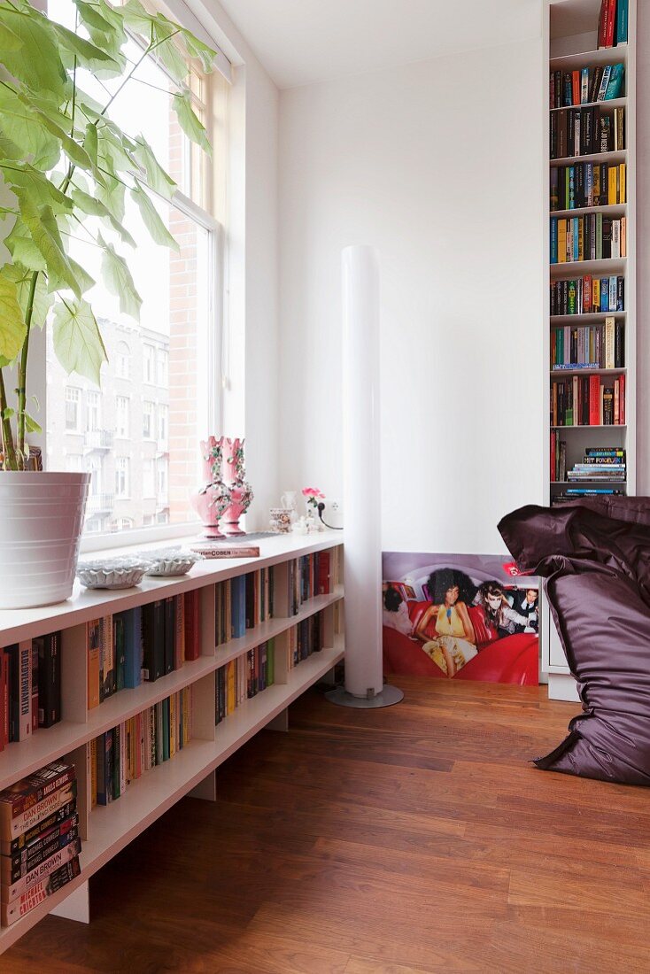 Bookshelves below window and narrow, cylindrical, white standard lamp in modern interior