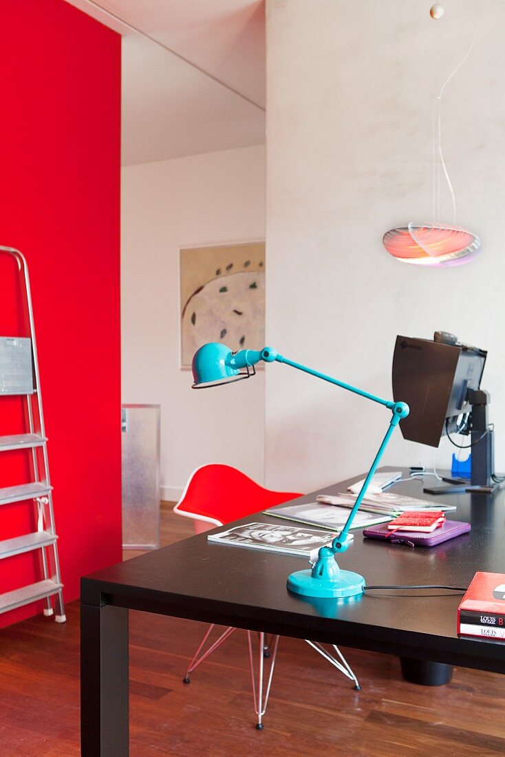 Hellblaue Retro Tischleuchte auf schwarzem Arbeitstisch, gegenüber rote Wand in modernem Ambiente