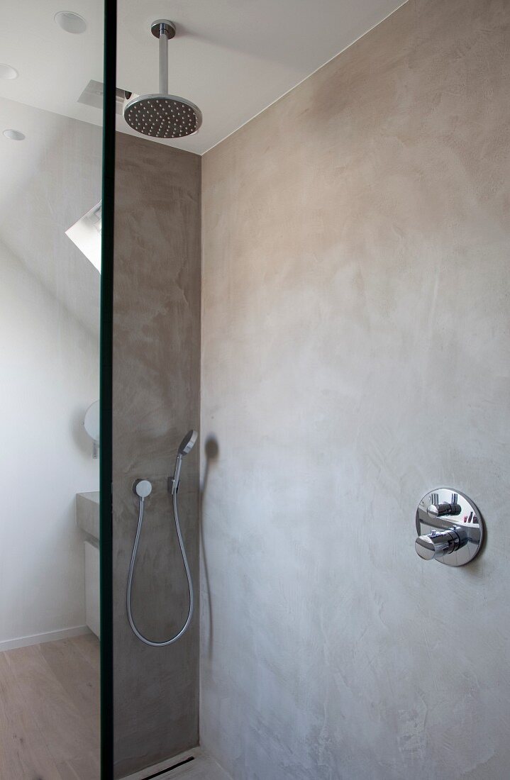 Rainfall shower and hand-held shower head in walk-in shower with marbled concrete walls and glass partition