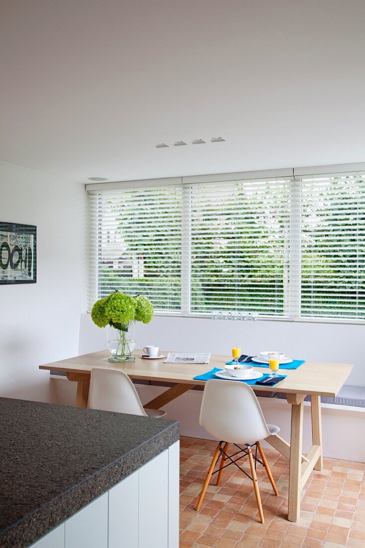 White, classic shell chairs, built-in window seat and simple wooden table; granite kitchen worksurface in foreground