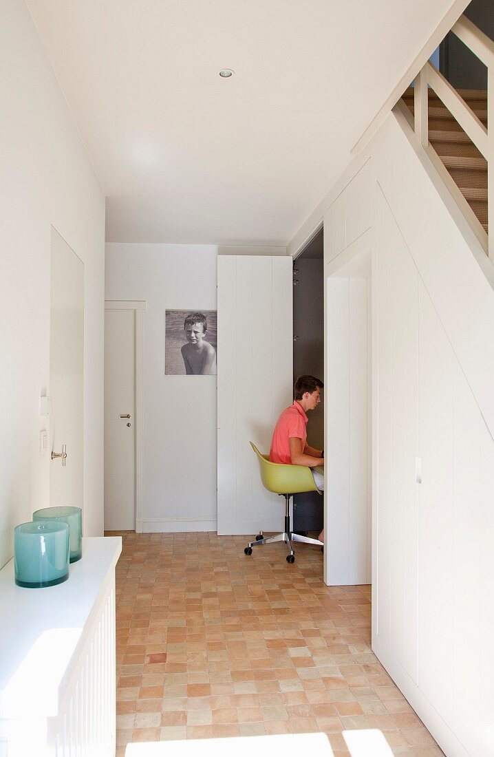 Teenager sitting on classic chair in workspace with folding door cleverly integrated under staircase in hallway