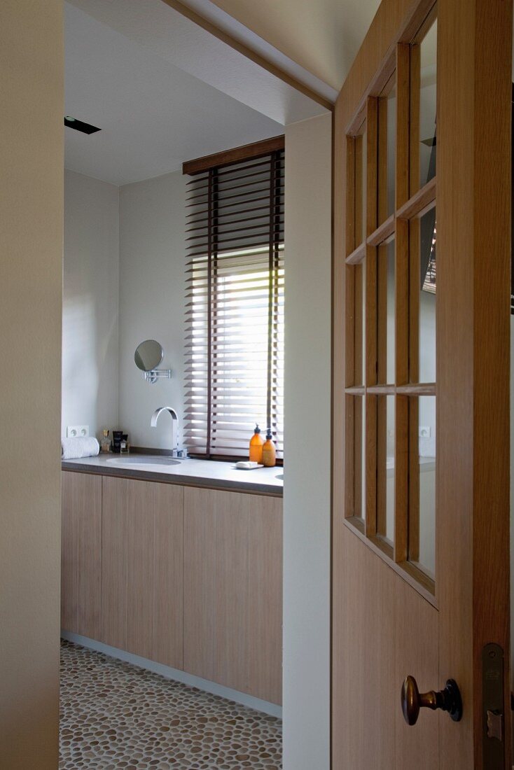Blick durch geöffnete Tür auf eingebauten Waschtisch vor Fenster mit Jalousie