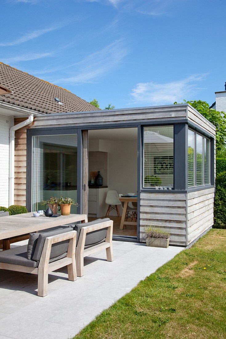 Holzverschalter, eingeschossiger Anbau für Wohnküche, davor ein Essplatz auf sonniger Terrasse