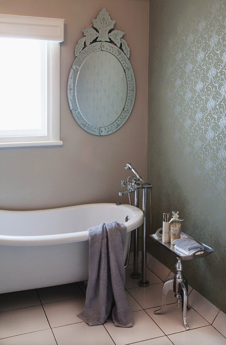 Ovaler Spiegel mit verziertem Metallrahmen und Vintage Badewanne mit Standarmatur im Bad mit Flüssigtapete an der Wand