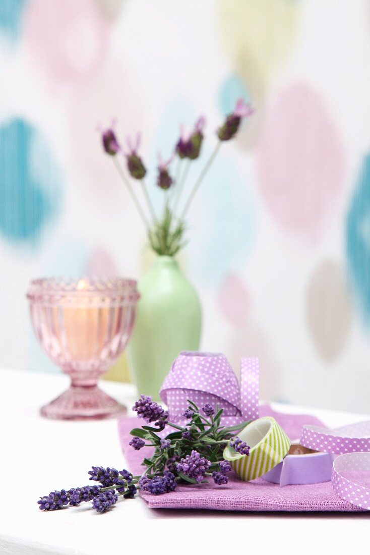 Lavendelzweige, Schleifenband und Masking Tape vor Kerze und Blumenvase mit Lavendelblüten