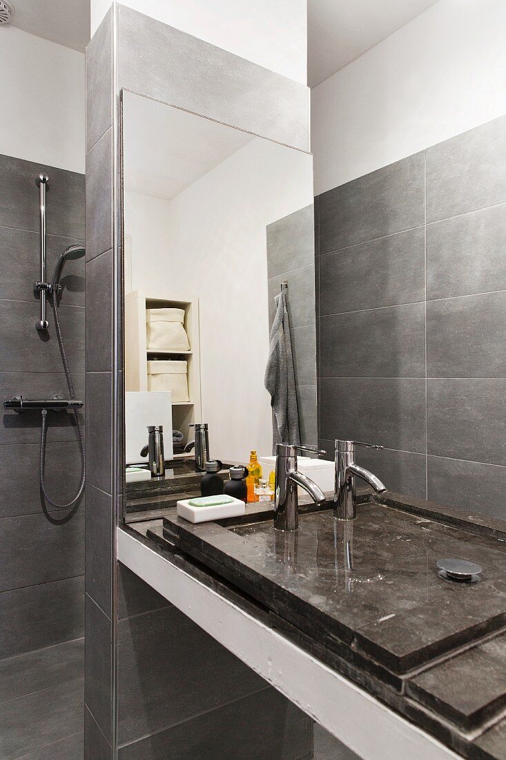 Grau gefliestes Designerbad mit minimalistischem Waschtisch an Mauerpfeiler mit Spiegel, vor Duschbereich