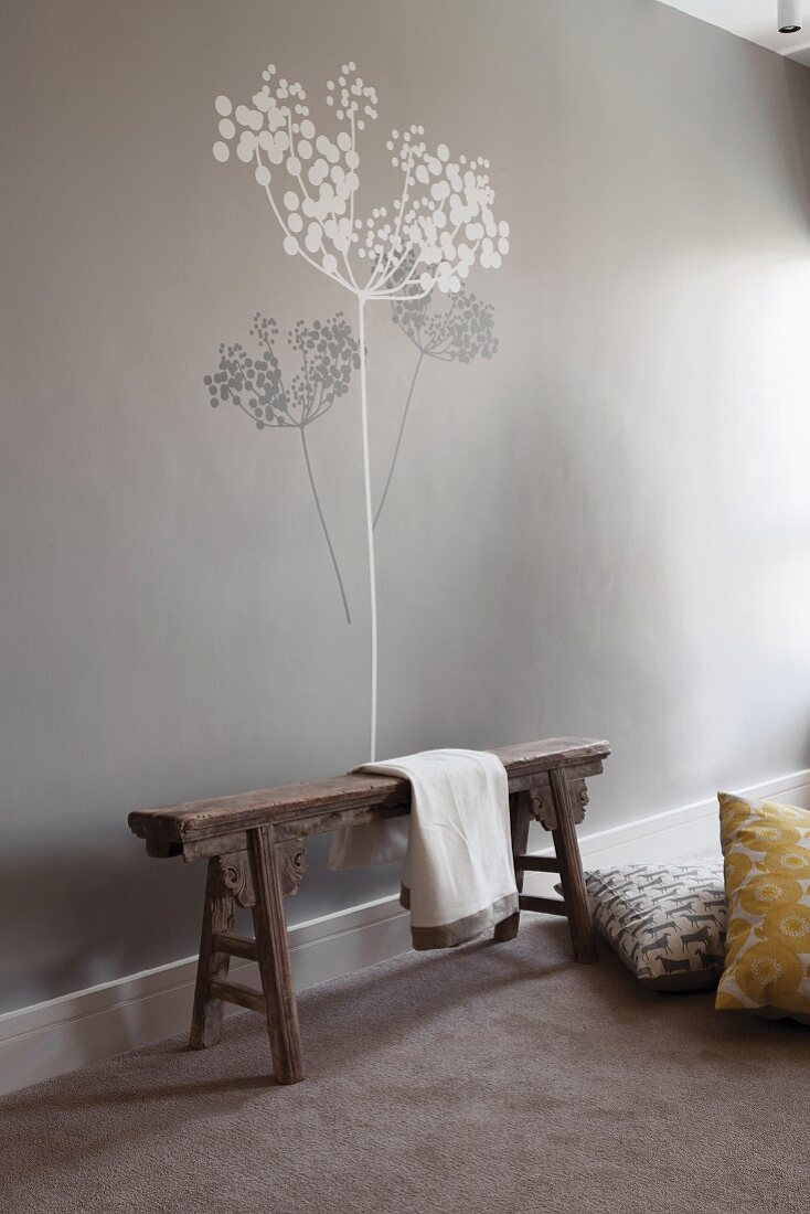 Rustic wooden bench against pale grey wall with tree mural in grey and white