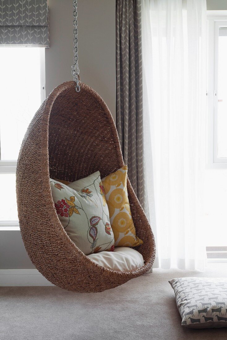 Comfortable wicker hanging chair in interior with walls painted pale grey