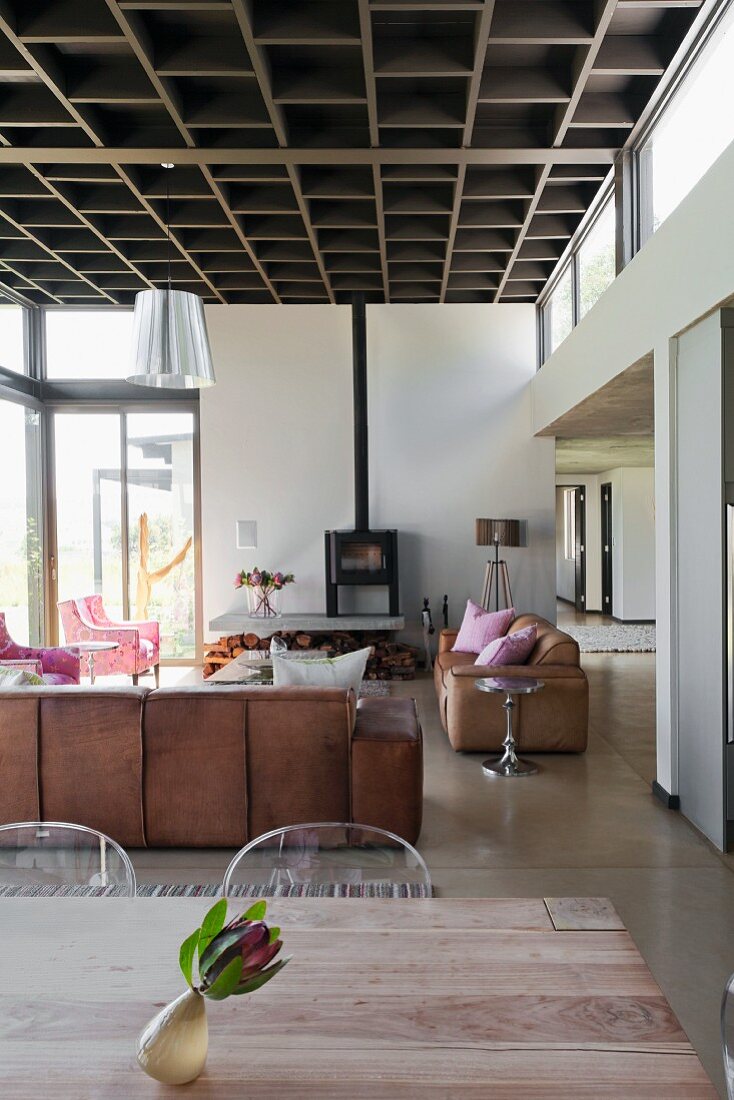 Blick über Tisch in Loungebereich mit Ledersofagarnitur und Kaminofen in loftartigem Wohnraum