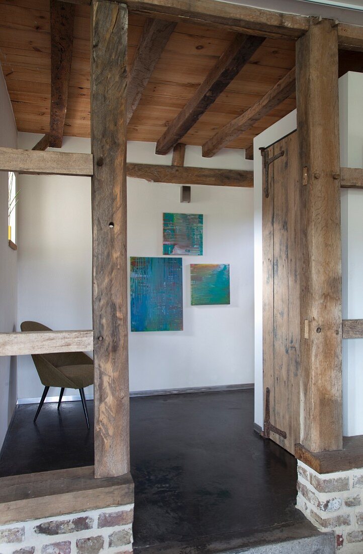 Doorway between wooden support pillars in foyer with rustic wooden ceiling and modern artworks