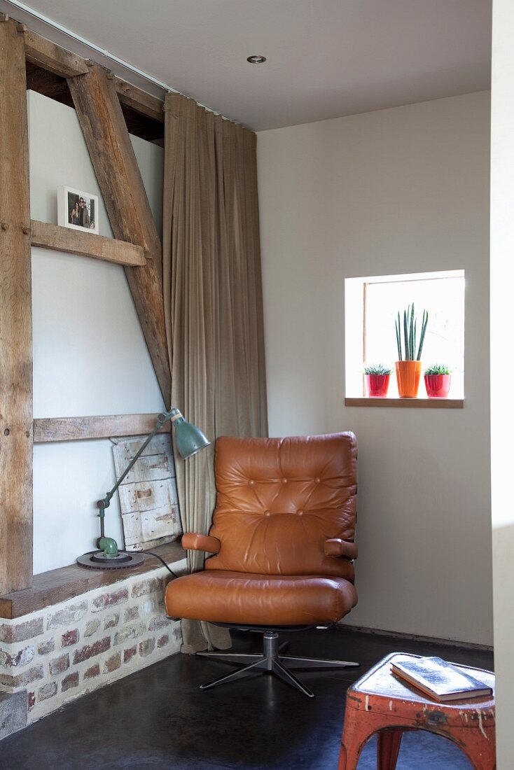 Brown leather armchair in corner and retro table lamp on masonry shelf in half-timbered wall