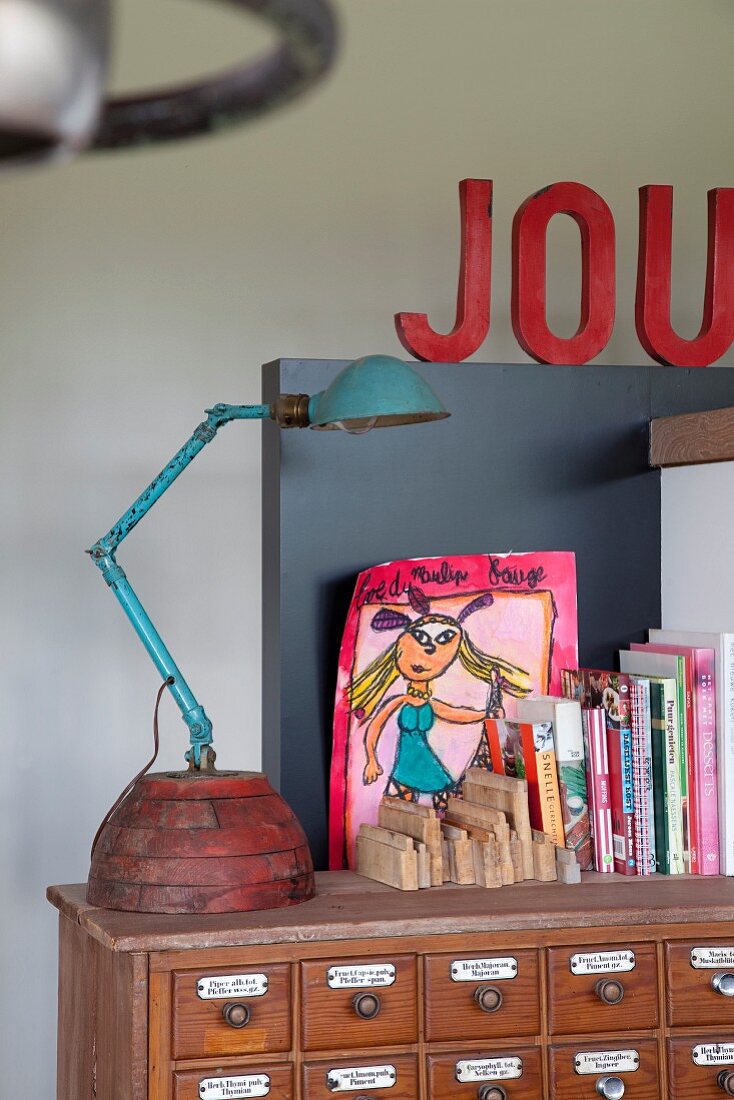 Turquoise, vintage table lamp, books and modern, colourful drawing on top of vintage apothecary cabinet